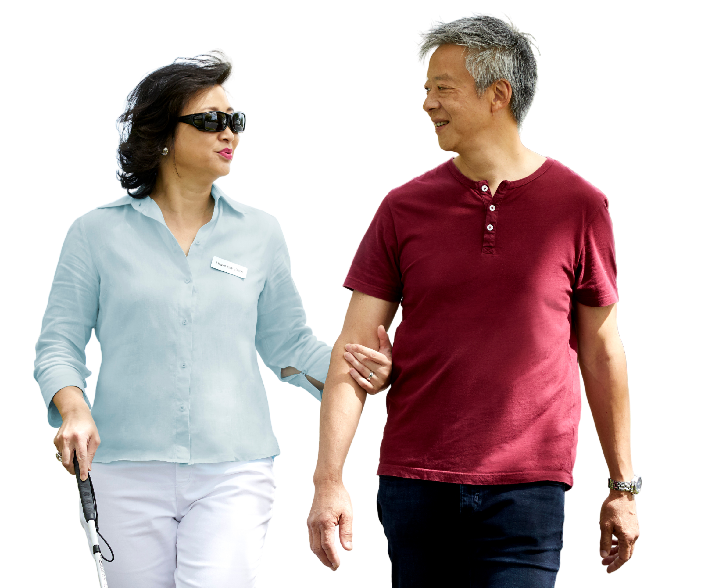 Client Karen and her partner walk confidently towards the camera, she holds her white cane in one hand and his arm in the other